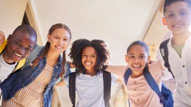 A group of children with backpacks are posing for a picture in a hallway.