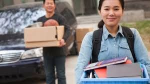 A man and a woman are carrying boxes and books to a car.