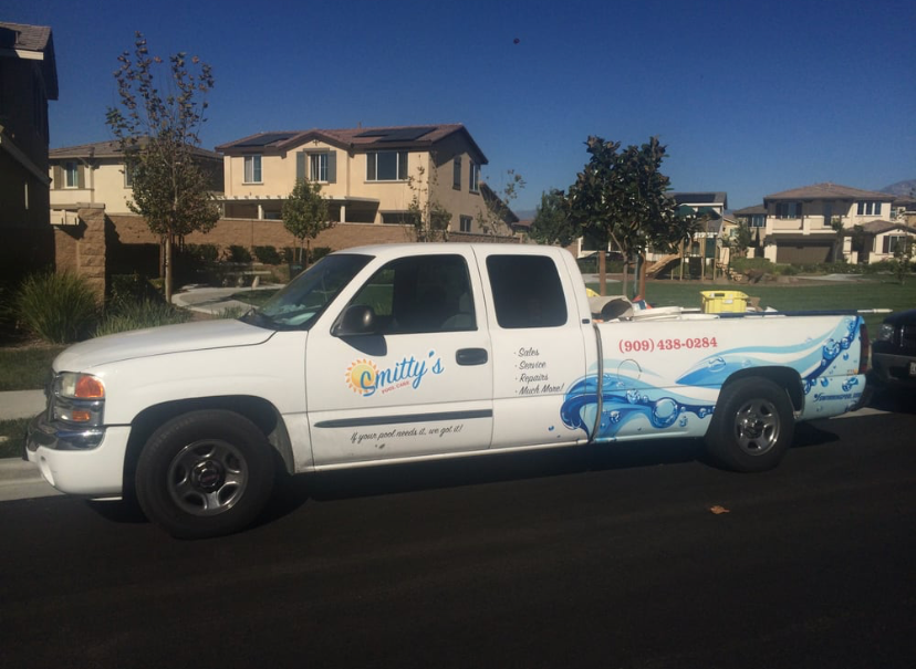 A white Smitty's pool service pickup truck parked on a suburban street.