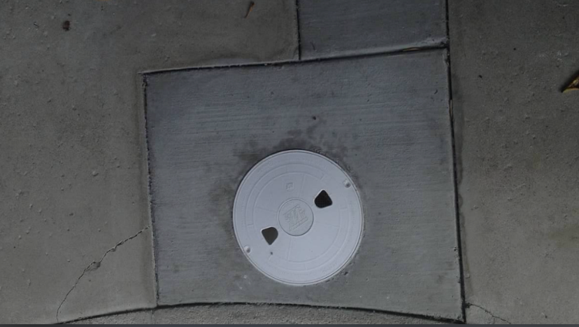 A circular utility cover centered within a square patch of concrete on a sidewalk.