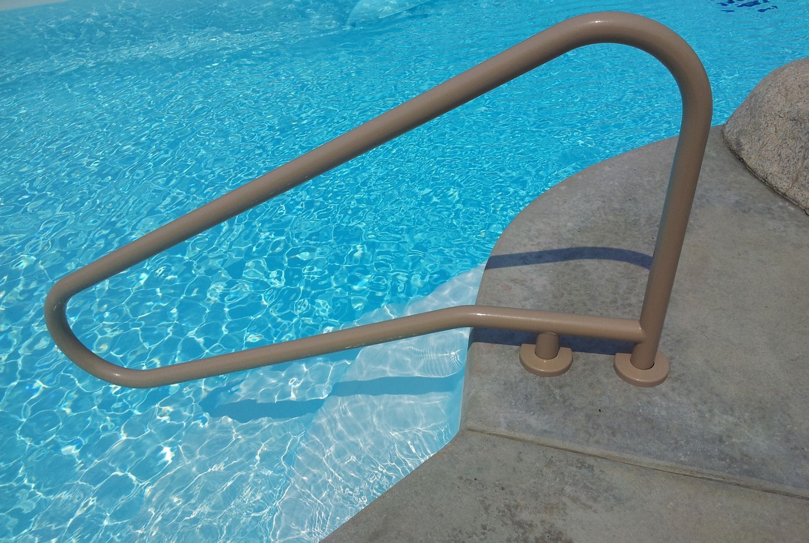 A person in a glove uses a long-handled net to remove debris from a bright blue, circular pool.