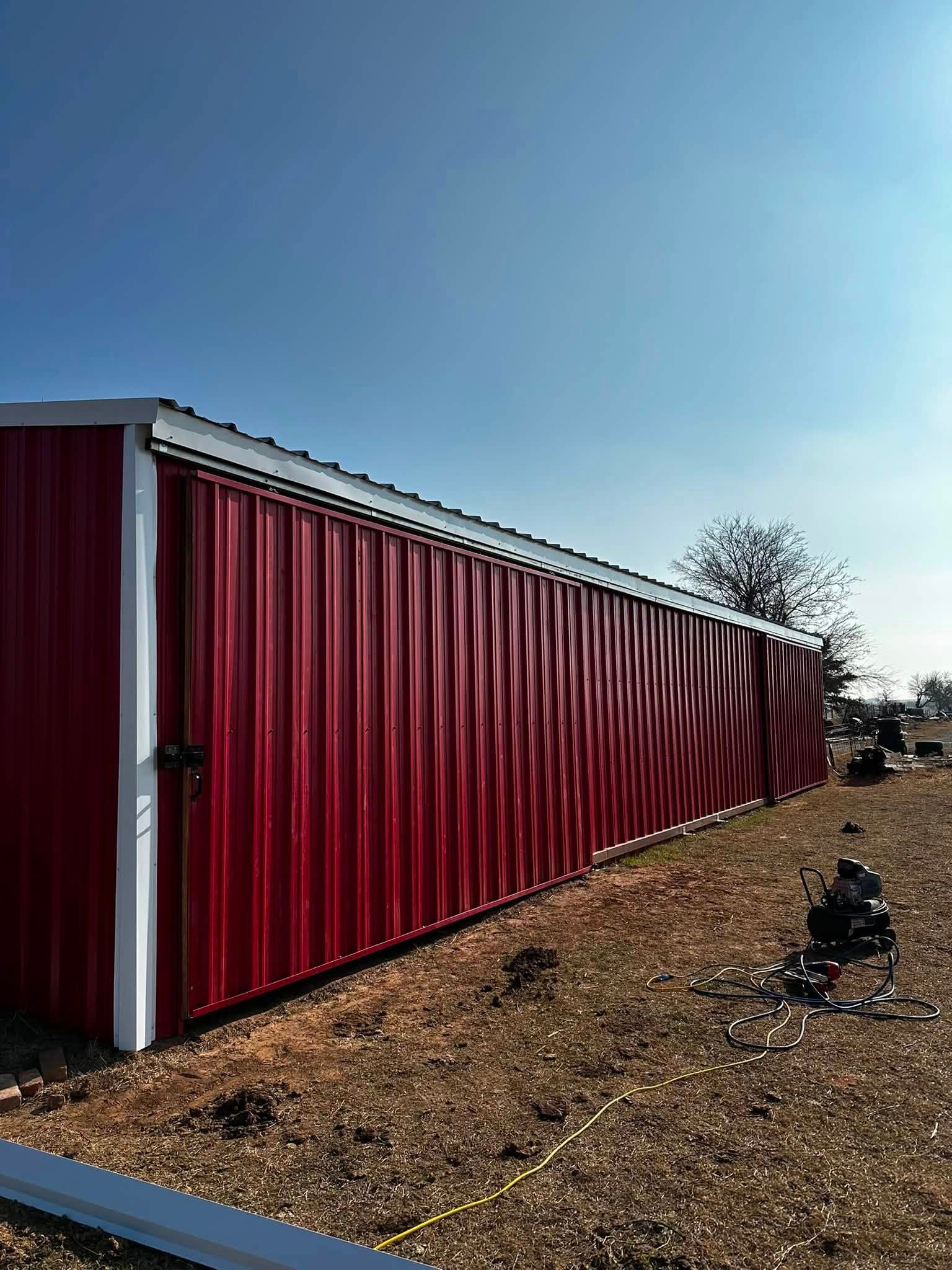 Red metal storage building with white trim beside a gravel lot under a clear blue sky