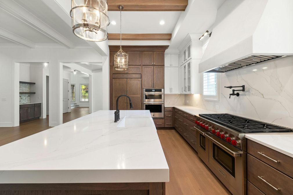 Modern white kitchen with dark wood cabinets, gas range, island, and pendant lights