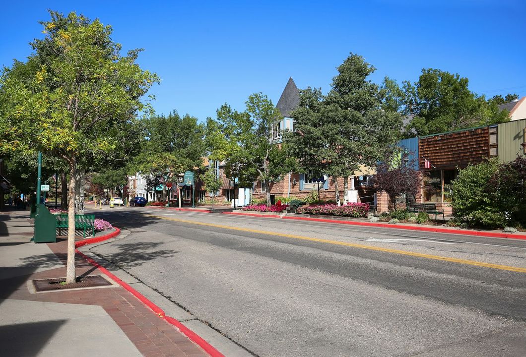 Tree-lined small-town street with red curb, brick buildings, and a clear blue sky