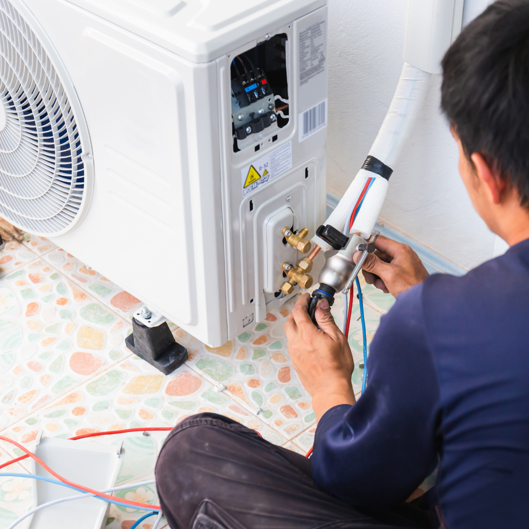 A man is sitting on the floor working on an air conditioner.