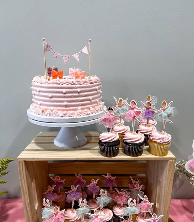 Cake and cupcakes on a wooden crate for a party. Pink cake with banner topper, fairy cupcake toppers.