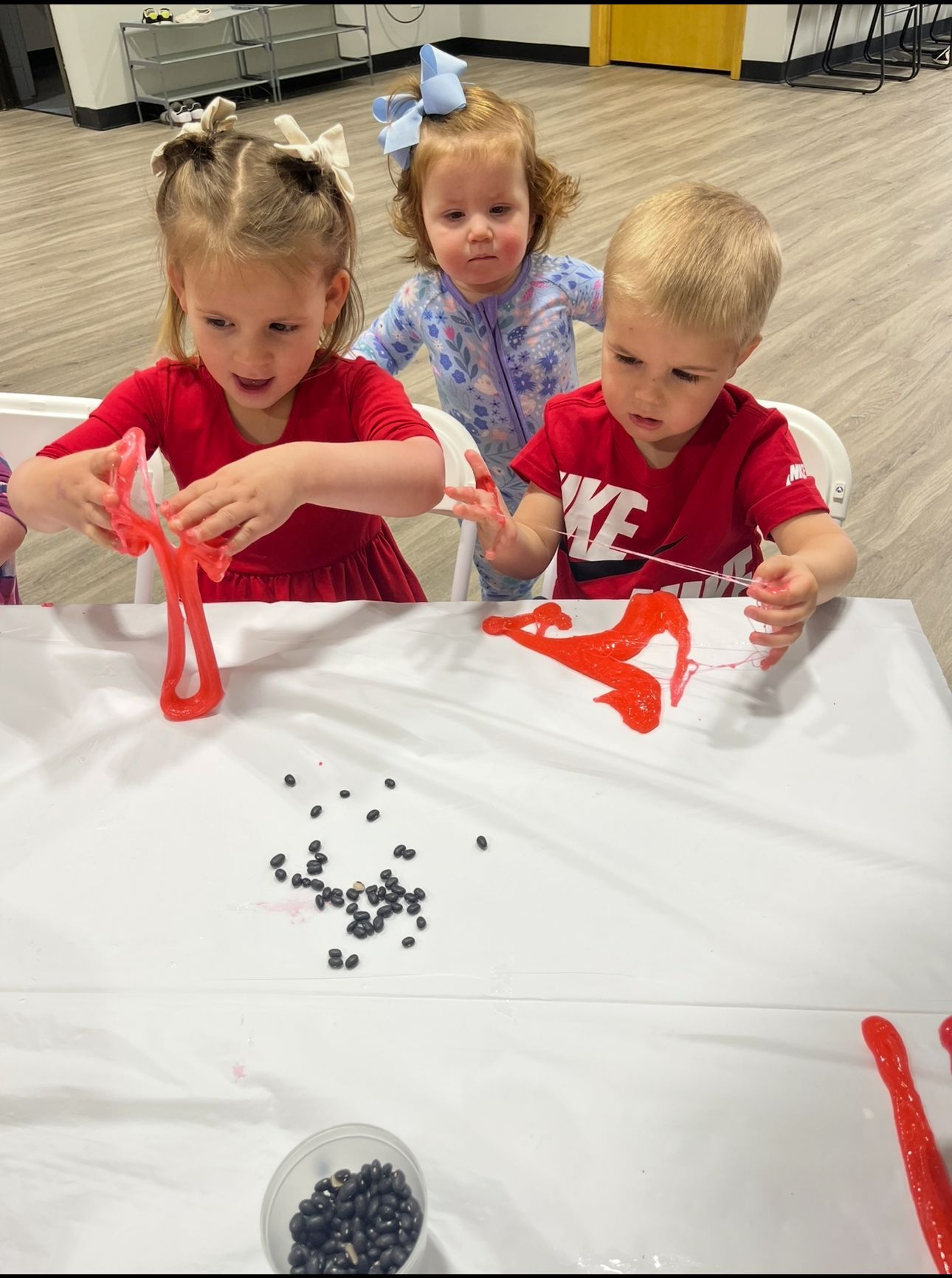 Three young children painting with red paint at a table.