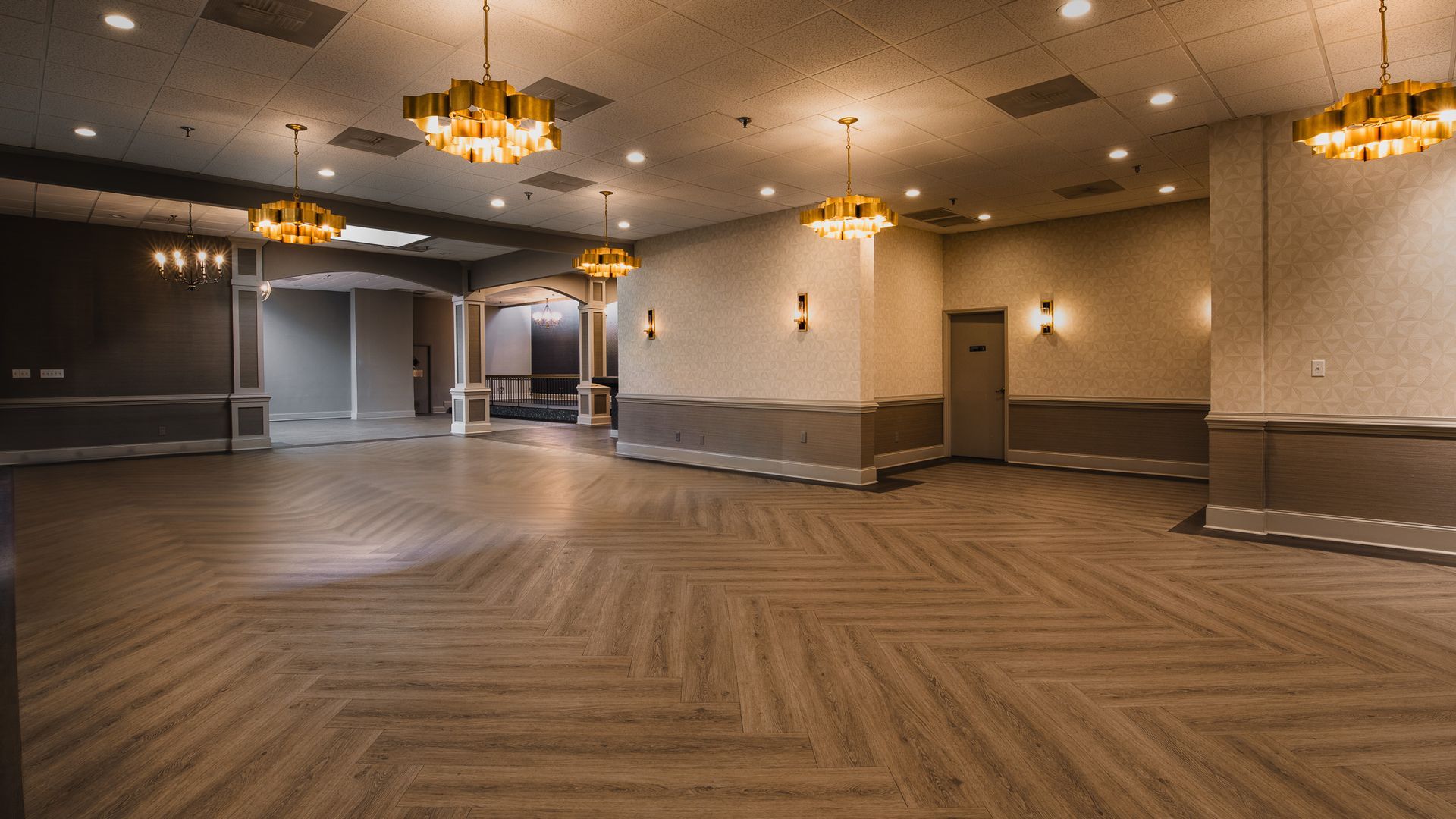 open wooden floor, chandeliers hanging from ceiling, bathroom door entrances against far wall
