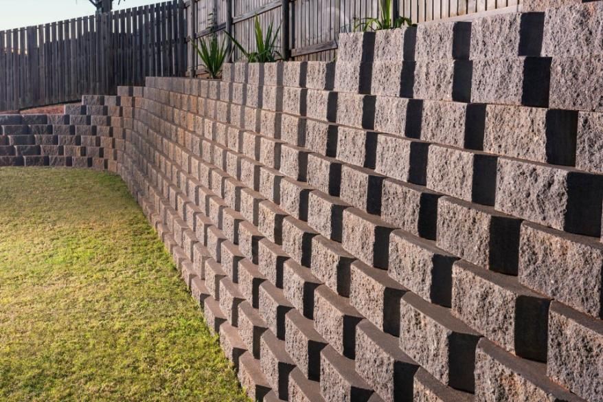 A Large Brick Wall Is Surrounded By Grass And A Fence — Southern Bricks & Pavers In Ulladulla, NSW