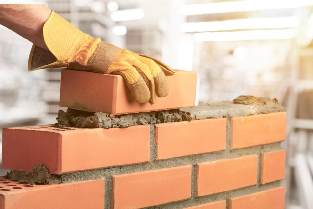 A Person Is Laying Bricks On Top Of A Brick Wall — Southern Bricks & Pavers In Sussex Inlet, NSW
