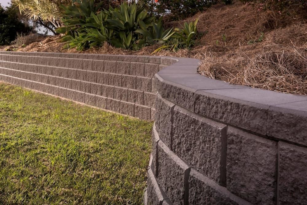 A Brick Wall Surrounds A Lush Green Lawn In A Backyard — Southern Bricks & Pavers In Ulladulla, NSW