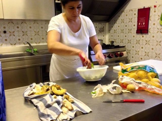 In una cucina professionale, una persona con una maglietta bianca prepara delle verdure, sbucciandole e mettendole in una ciotola bianca su un bancone di metallo.