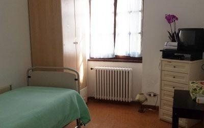 Una camera da letto con un letto, un alto armadio in legno, un termosifone sotto una finestra e una cassettiera con televisore e una pianta.