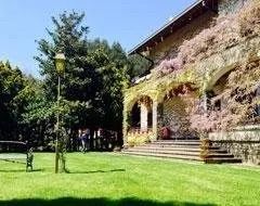Una casa in pietra con piante rampicanti fiorite sorge accanto a un prato con un alto lampione sotto un cielo azzurro e limpido.
