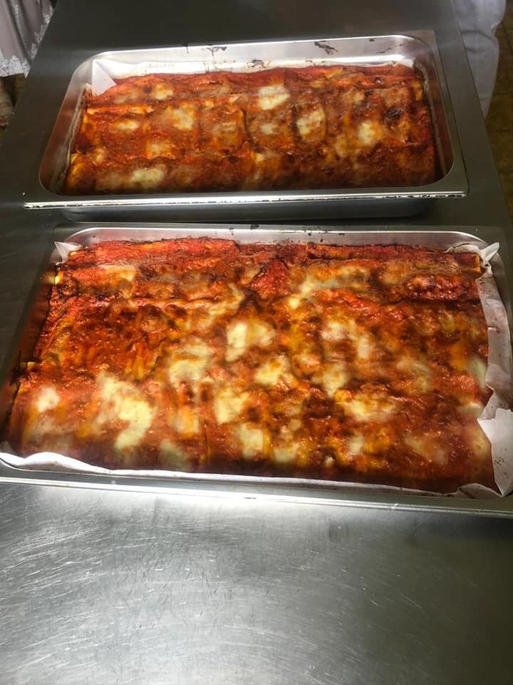 Due vassoi rettangolari di metallo pieni di lasagne appena sfornate, ricoperte di formaggio e salsa di pomodoro