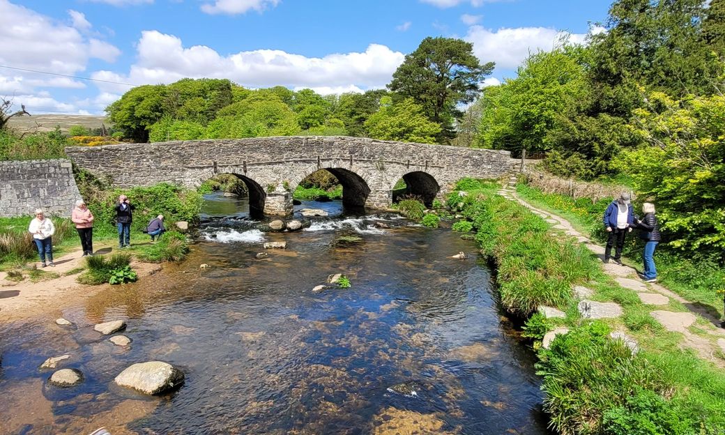 Ancient stone bridge on Dartmoor, Devon, UK with guests from a private tour enjoying the clear water and spotting fish.