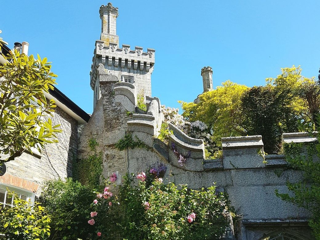 A tall tower and crenellated walls with lush flowering shrubs and a blue sky in Fowey