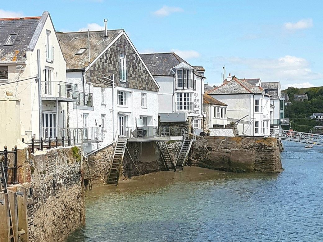 Old white-painted buildings next to the river at low tide by Town Quay in Fowey part of a custom tour