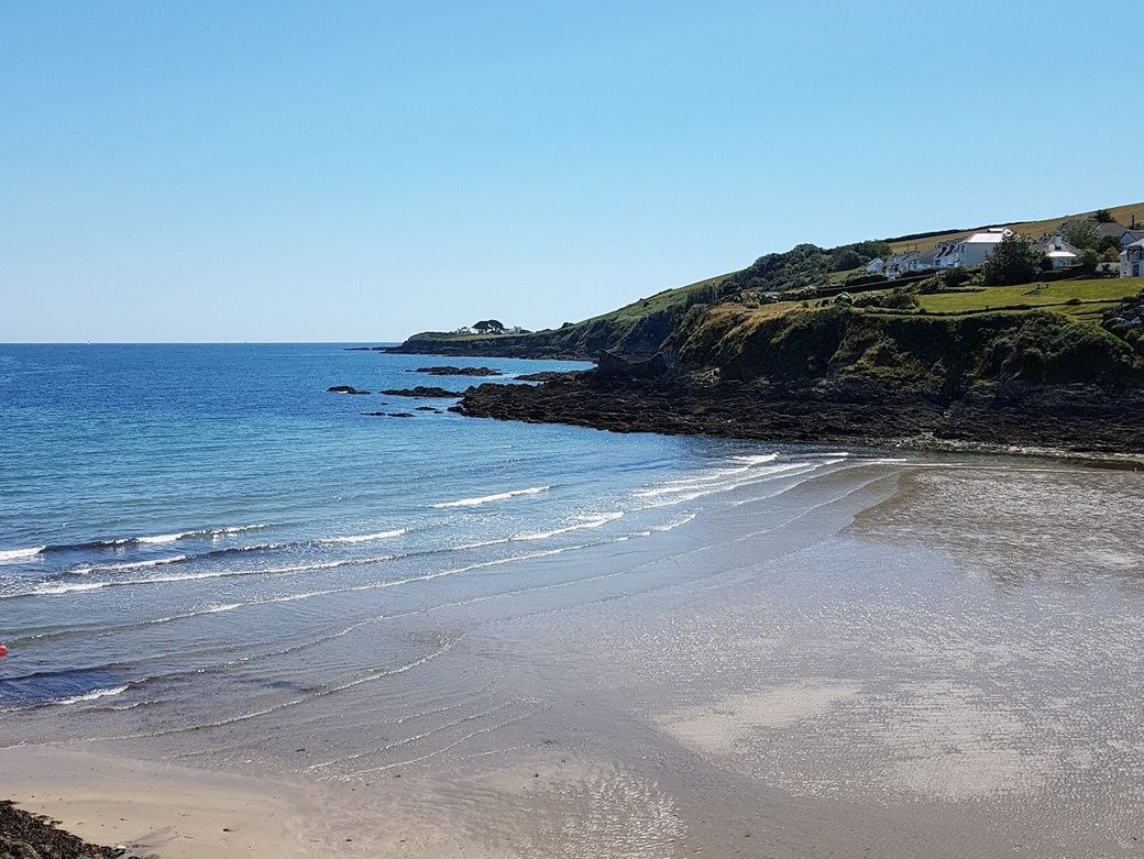 Sandy beach with blue sea and waves rolling in and a rocky headland beyond at Portmellon