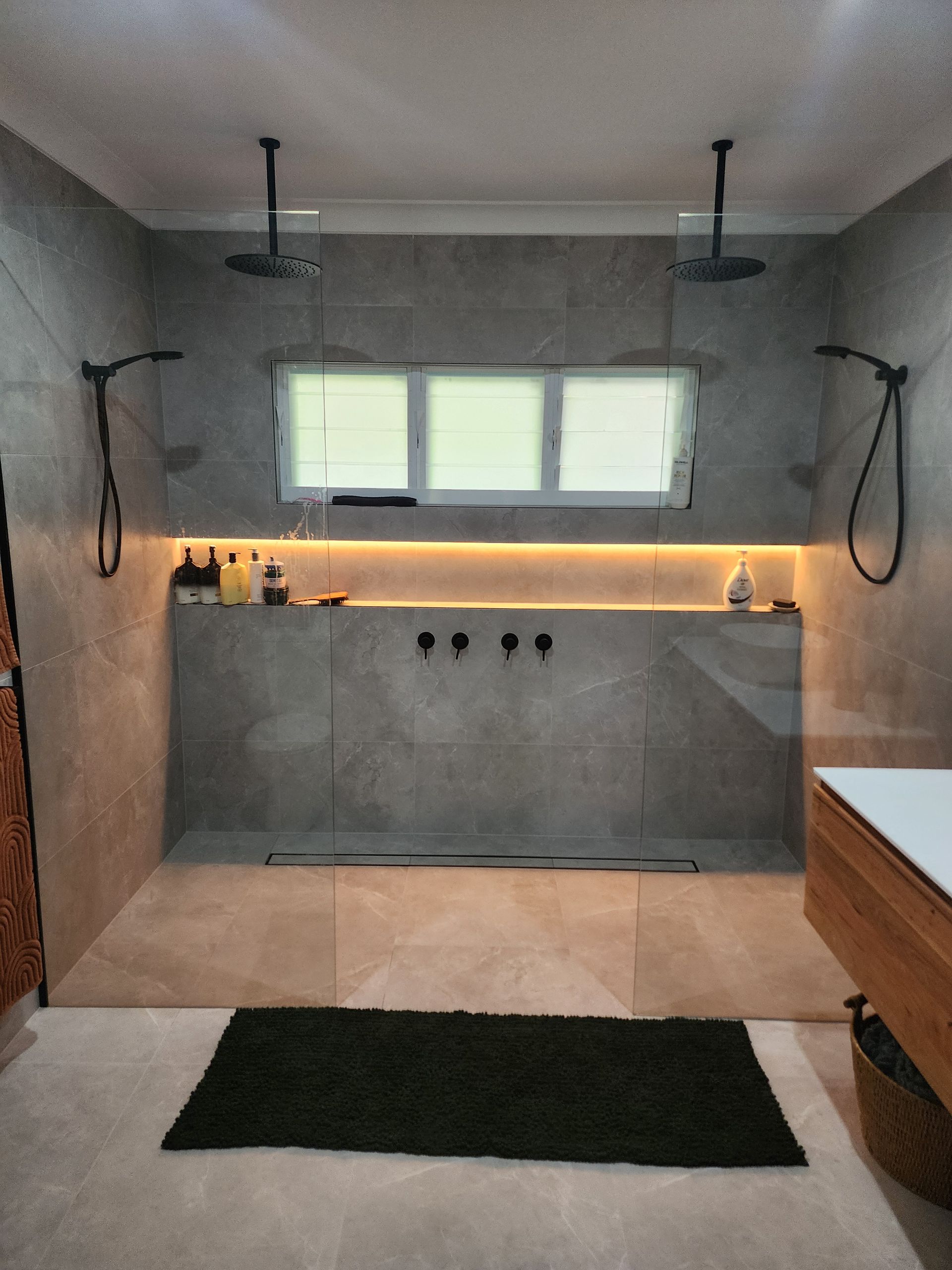 Modern bathroom with tiled shower, double window, wall lights, and a dark bath mat