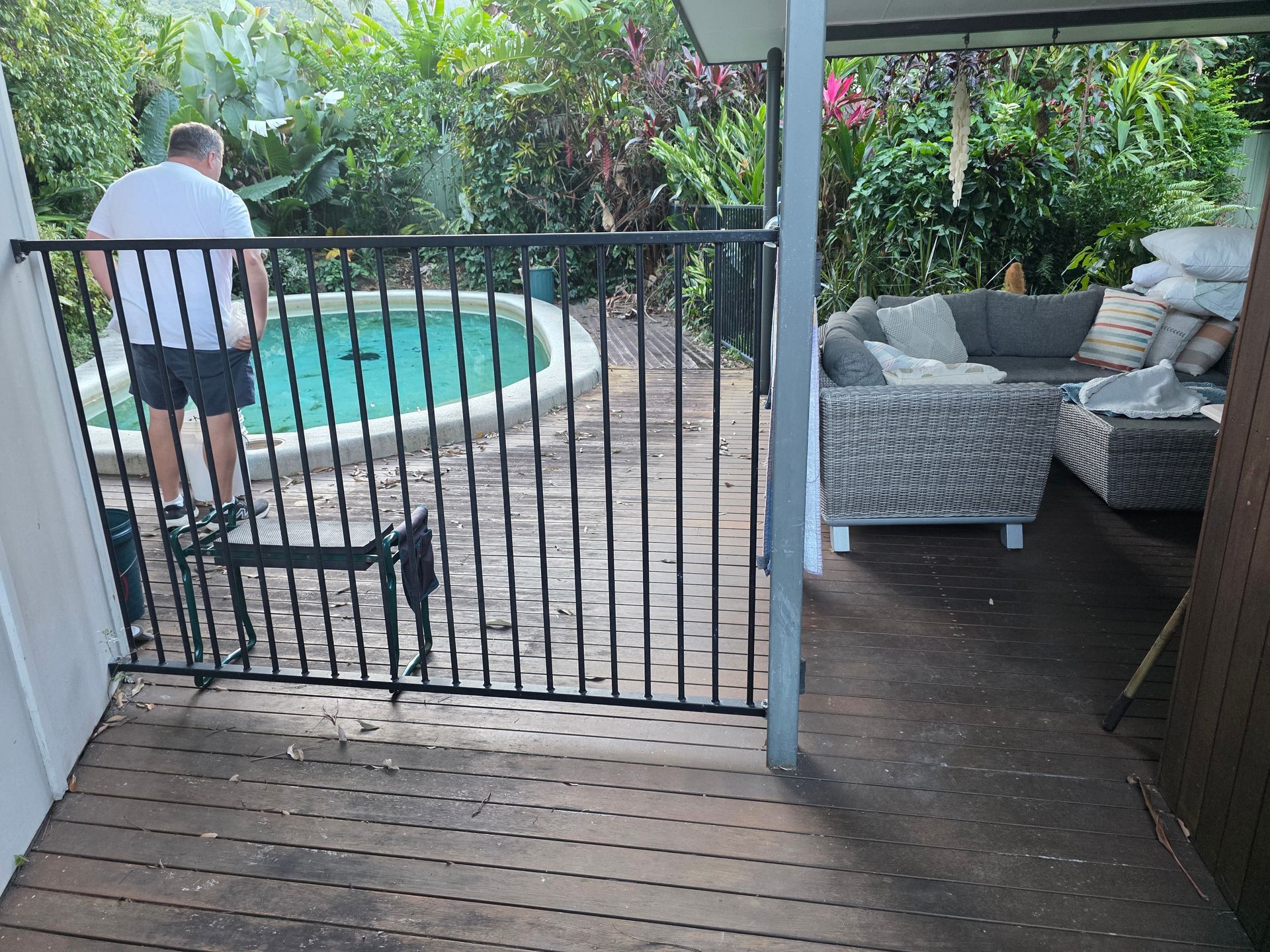 Back patio with a gated pool area and wicker seating; a person stands by the pool.