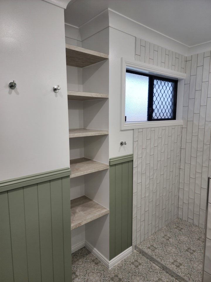 Small tiled bathroom with built-in shelves, green wainscoting, and a frosted window.