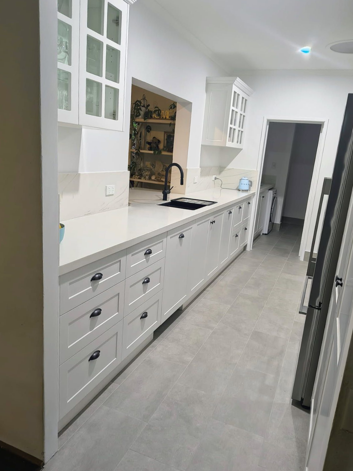 Bright white kitchen hallway with long cabinets, sink, and gray floor tiles