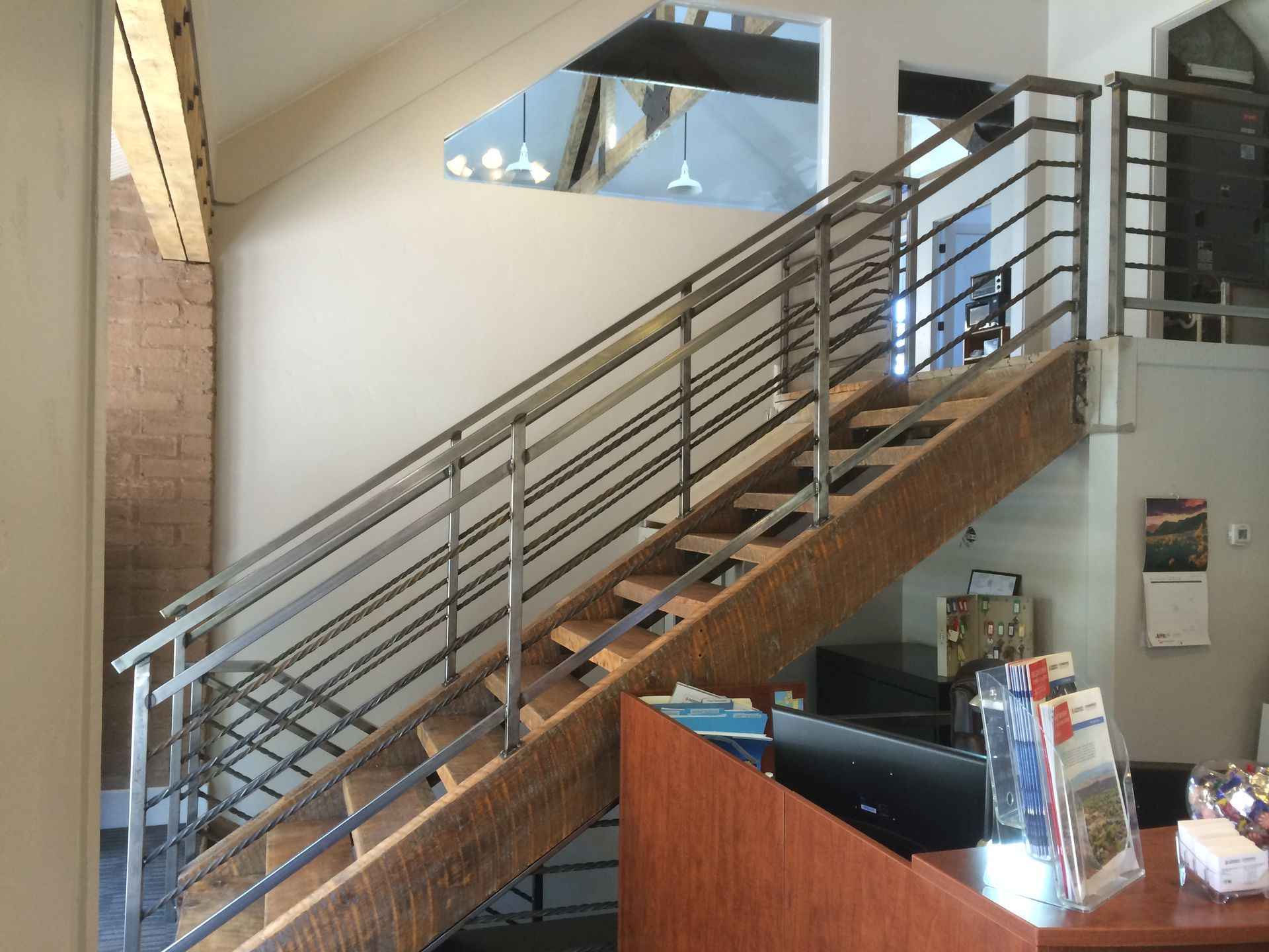 A wooden staircase with metal railings leads to an upper level in a brightly lit, modern office or lobby area.