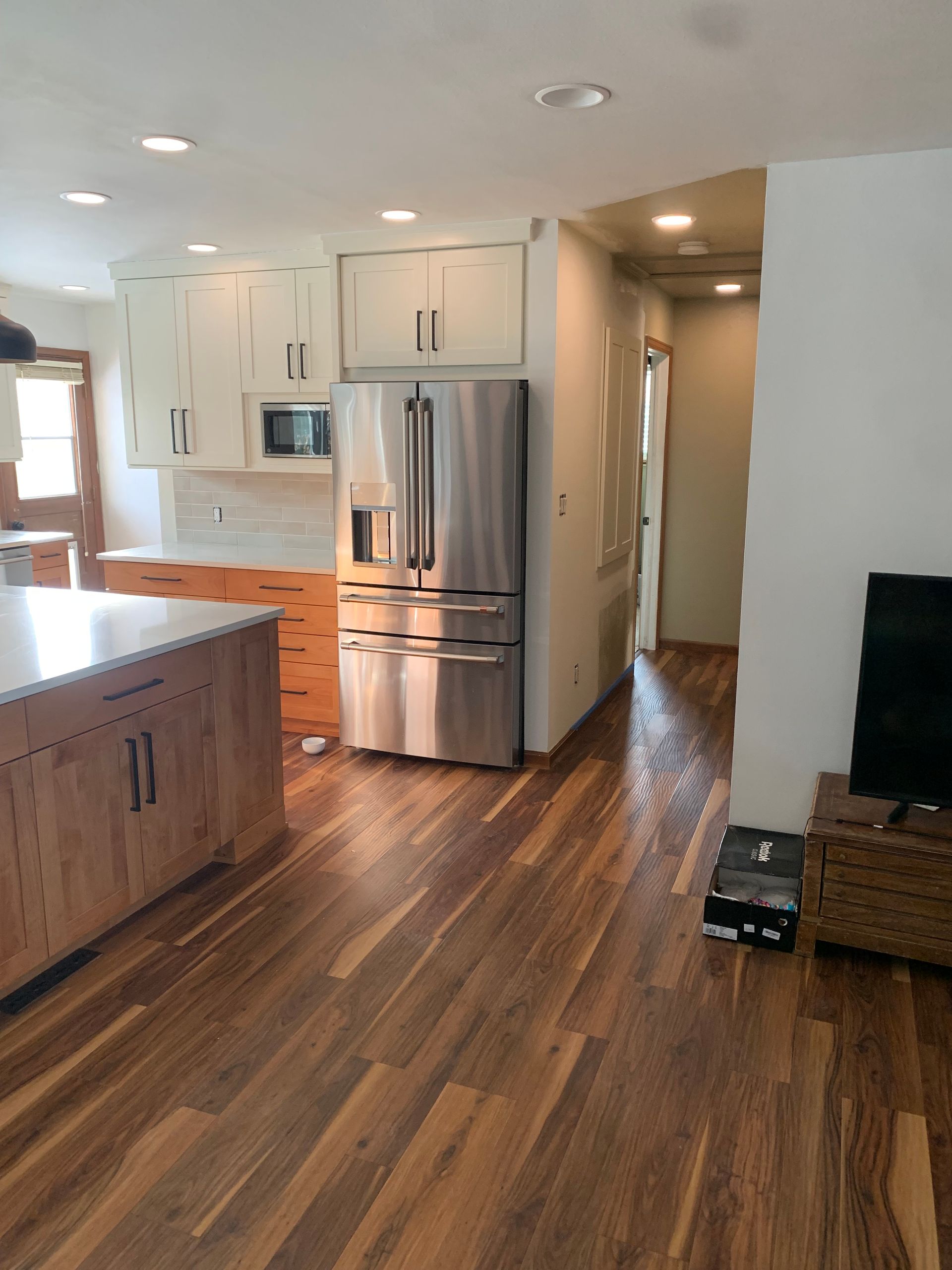 Kitchen featuring white cabinets, wood lower cabinets, a stainless steel refrigerator, and wood flooring.