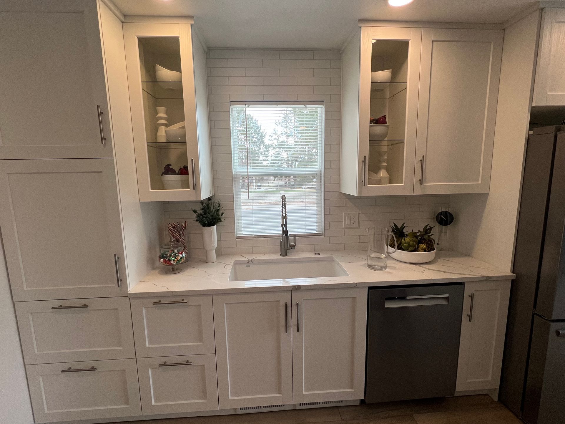 A modern kitchen featuring white cabinets, a sink under a window, subway tile backsplash, and a stainless steel dishwasher.