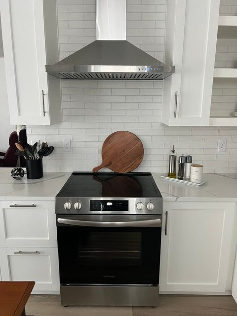 A stainless steel stove and range hood between white cabinets and a white subway tile backsplash in a modern kitchen.