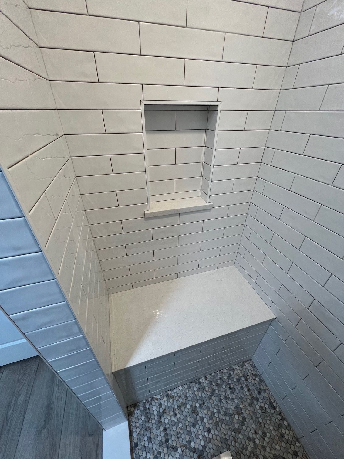 A shower stall with white subway tiles, a built-in stone bench, a recessed niche, and a stone pebble floor.
