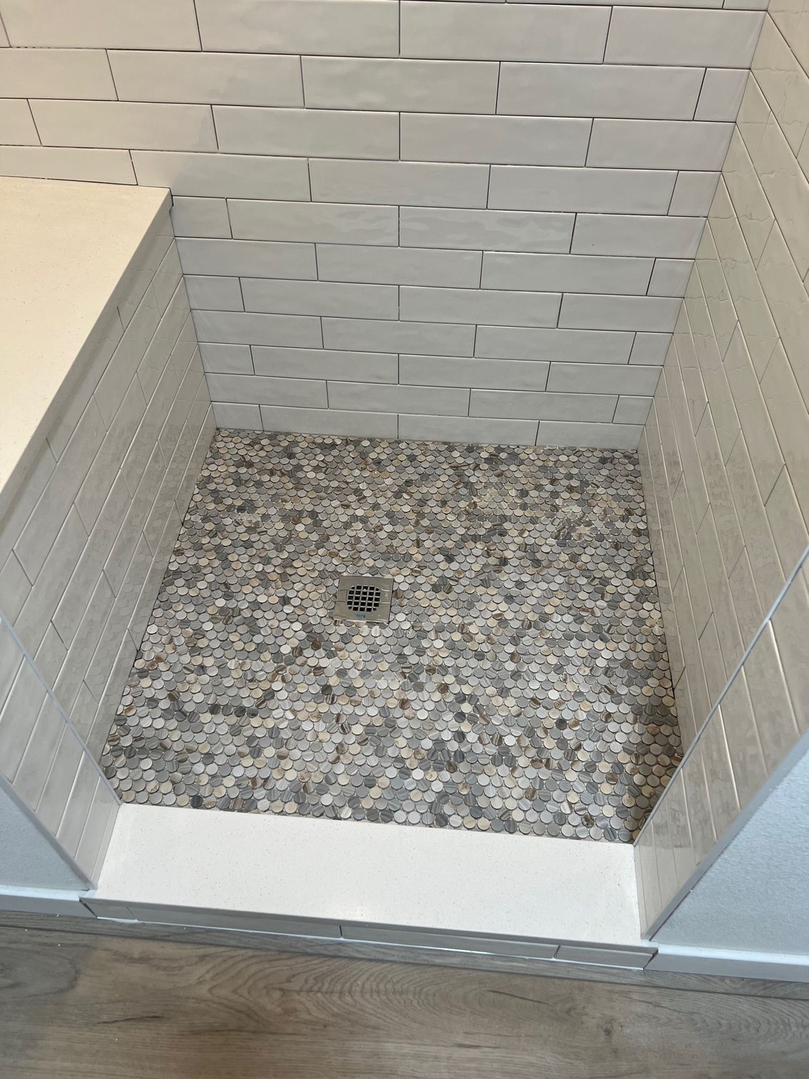 A walk-in shower with white rectangular subway tile walls, a pebble-textured floor, and a solid white threshold.