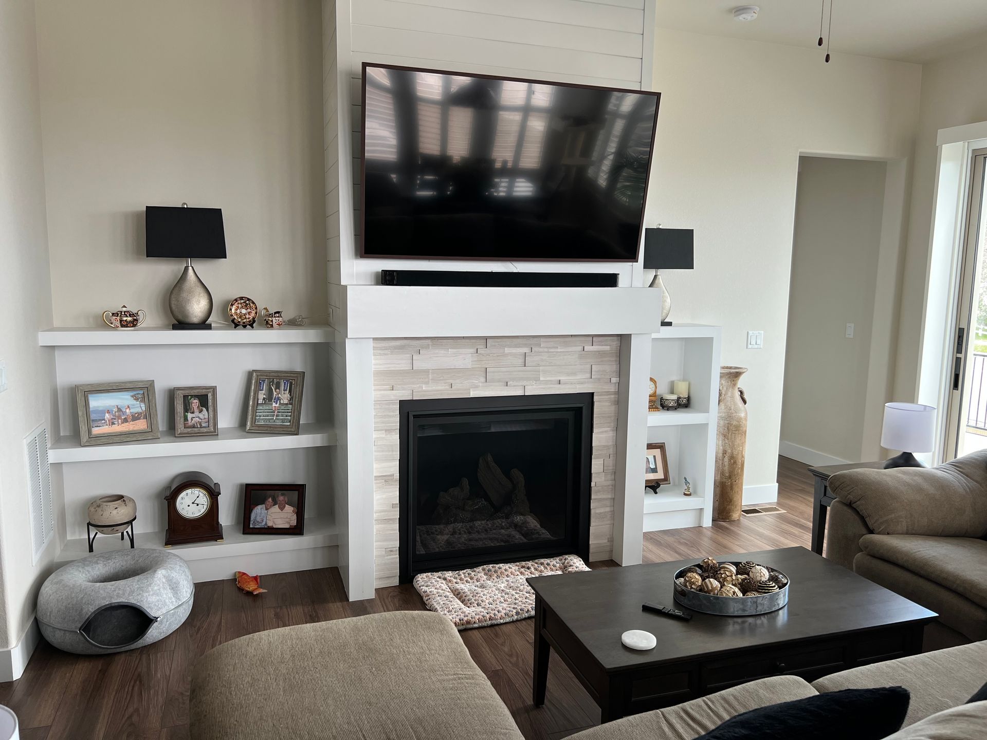 A living room featuring a stone fireplace with a mounted television, flanked by white built-in shelves displaying decor.