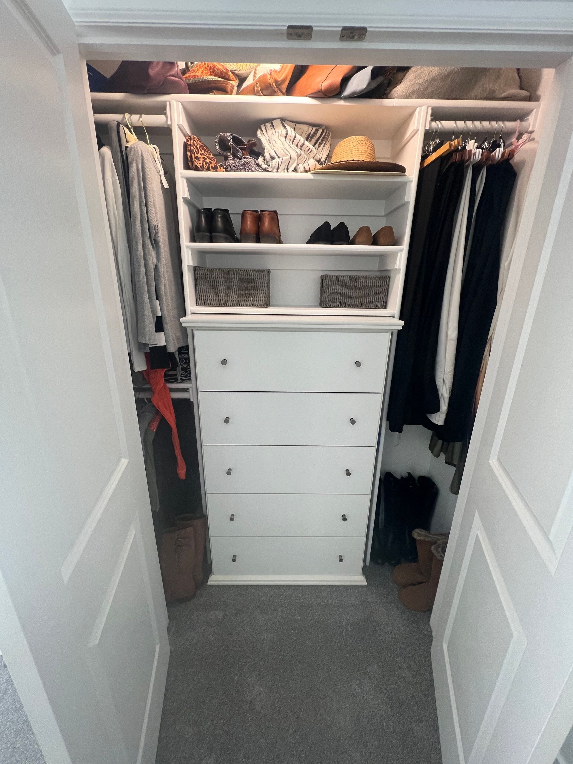 A small closet featuring a white chest of drawers, shelving with shoes and accessories, and hanging clothes on both sides.