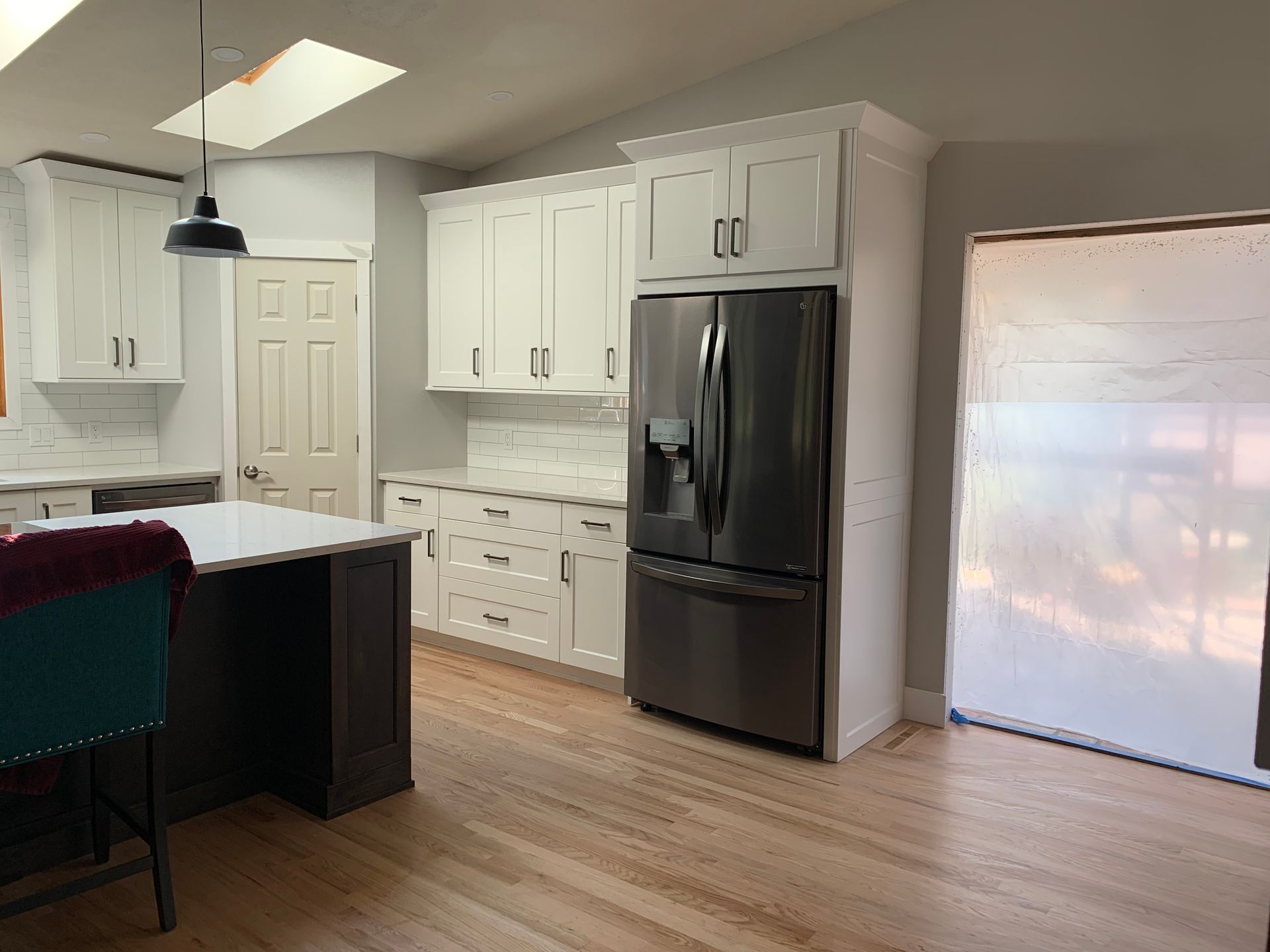 A modern kitchen featuring white cabinets, stainless steel appliances, a dark kitchen island, and light wood flooring.