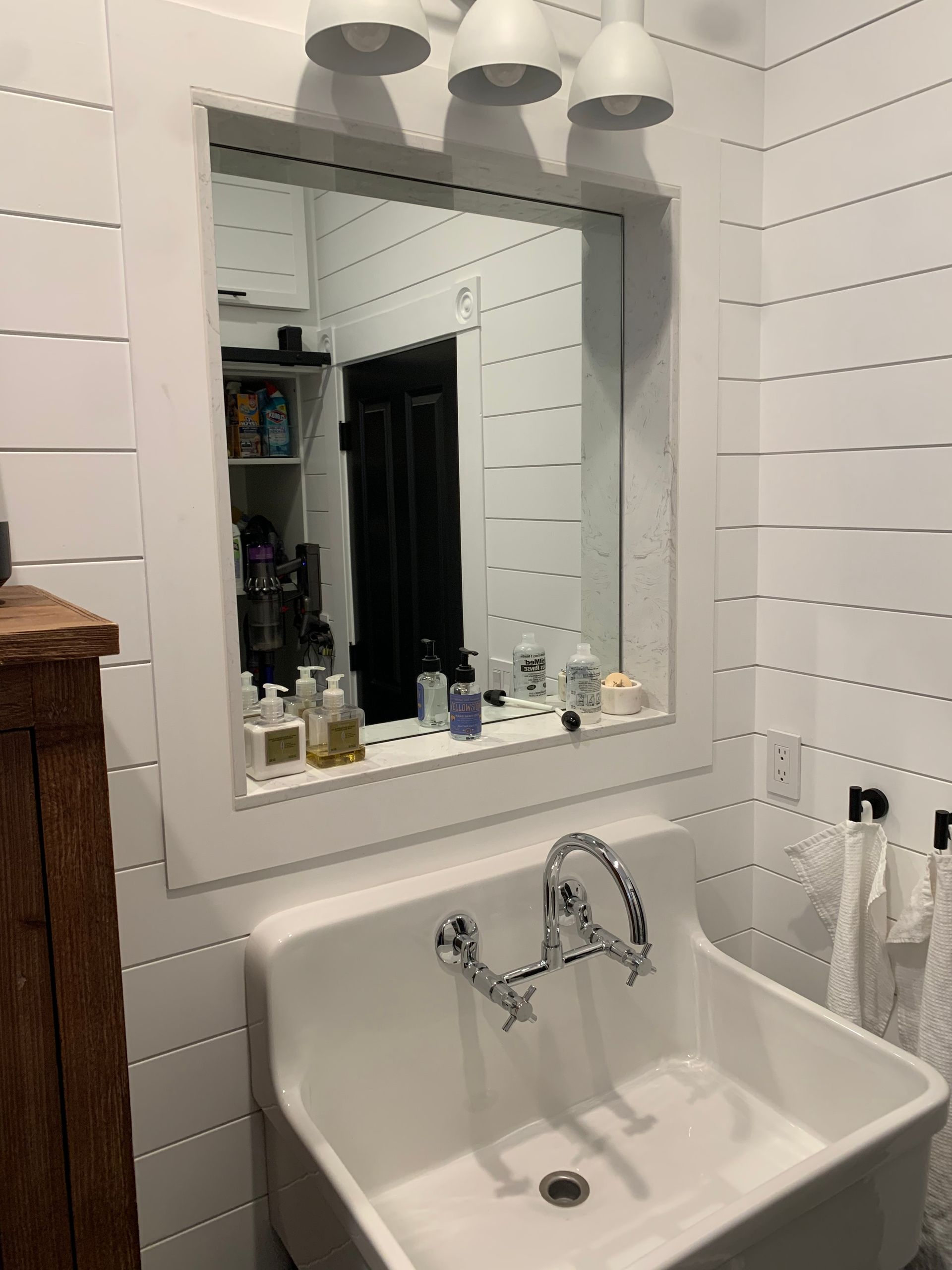A white farmhouse-style sink with a chrome wall-mounted faucet, set against white shiplap walls with a framed mirror.