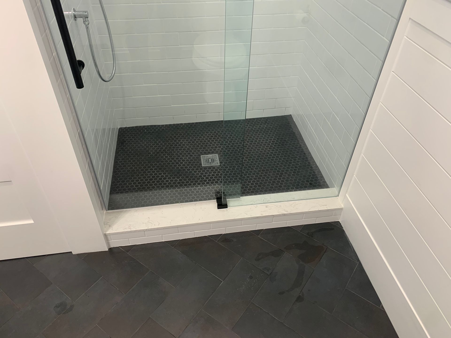 A glass-door shower with dark, textured tile flooring, white subway tile walls, and a white base in a modern bathroom.