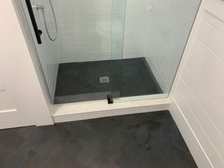A glass-enclosed shower with dark gray pebble flooring, white subway tile walls, and a white threshold.