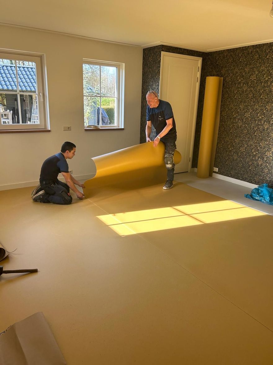 Een persoon knielt op een houten vloer en meet en legt laminaatplanken in een lichte woonkamer.
