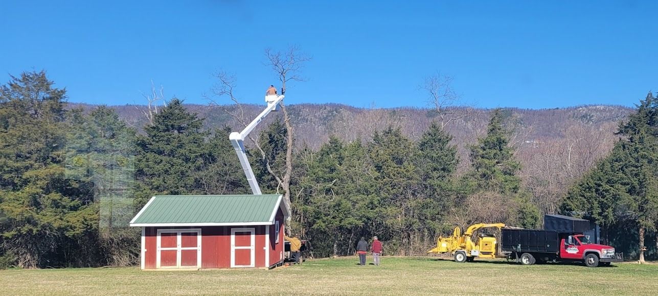 Red shed and tall crane in a grassy field with mountains, trees, and parked vehicles nearby