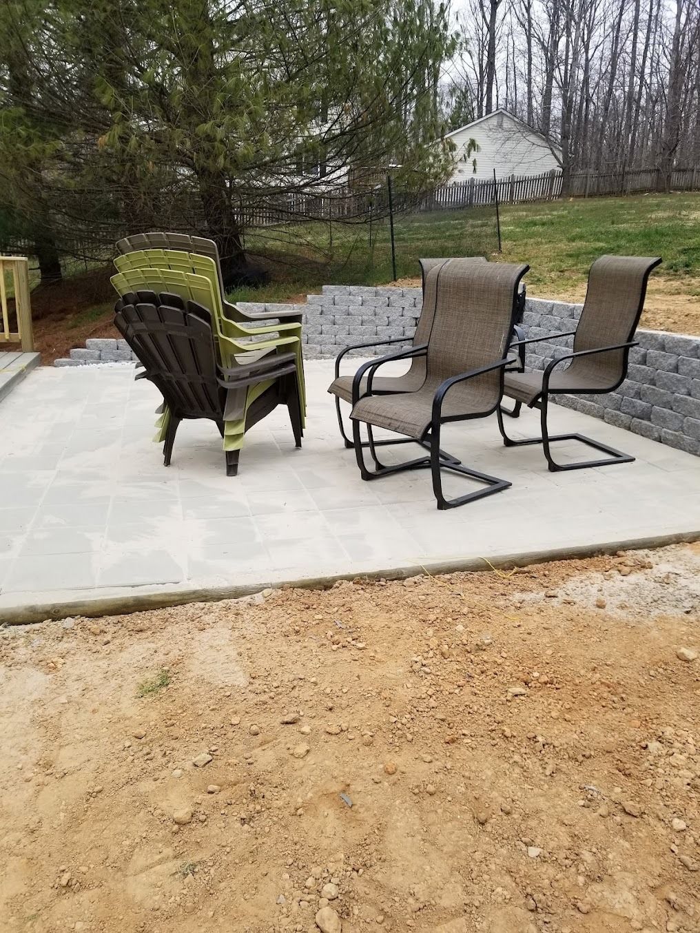 Patio with three outdoor chairs on a concrete slab beside a gravel yard and trees