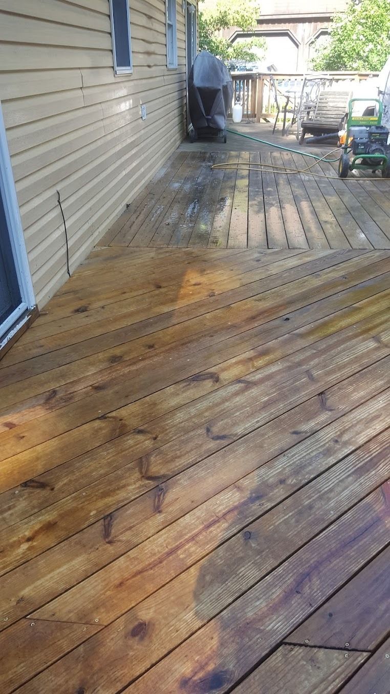 Weathered wooden deck beside a house, wet in spots, leading to a backyard with a grill and railing.