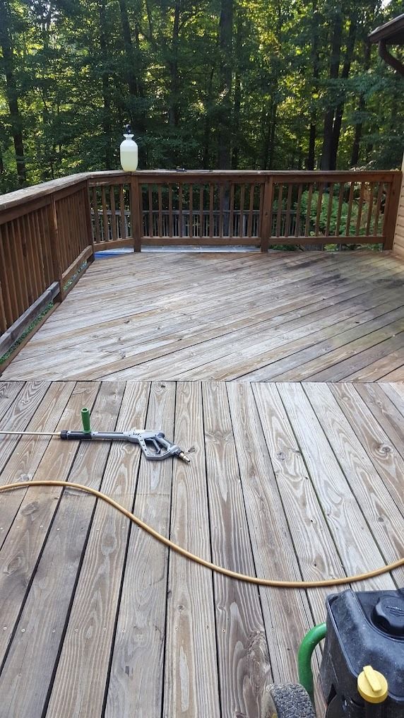 Wooden deck with railings in a wooded backyard, with a hose and power tool on the floor.