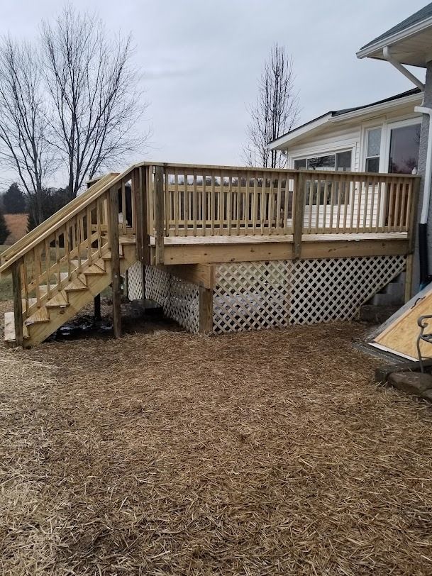 Wooden backyard deck with stairs and railing beside a house, over lattice skirting.