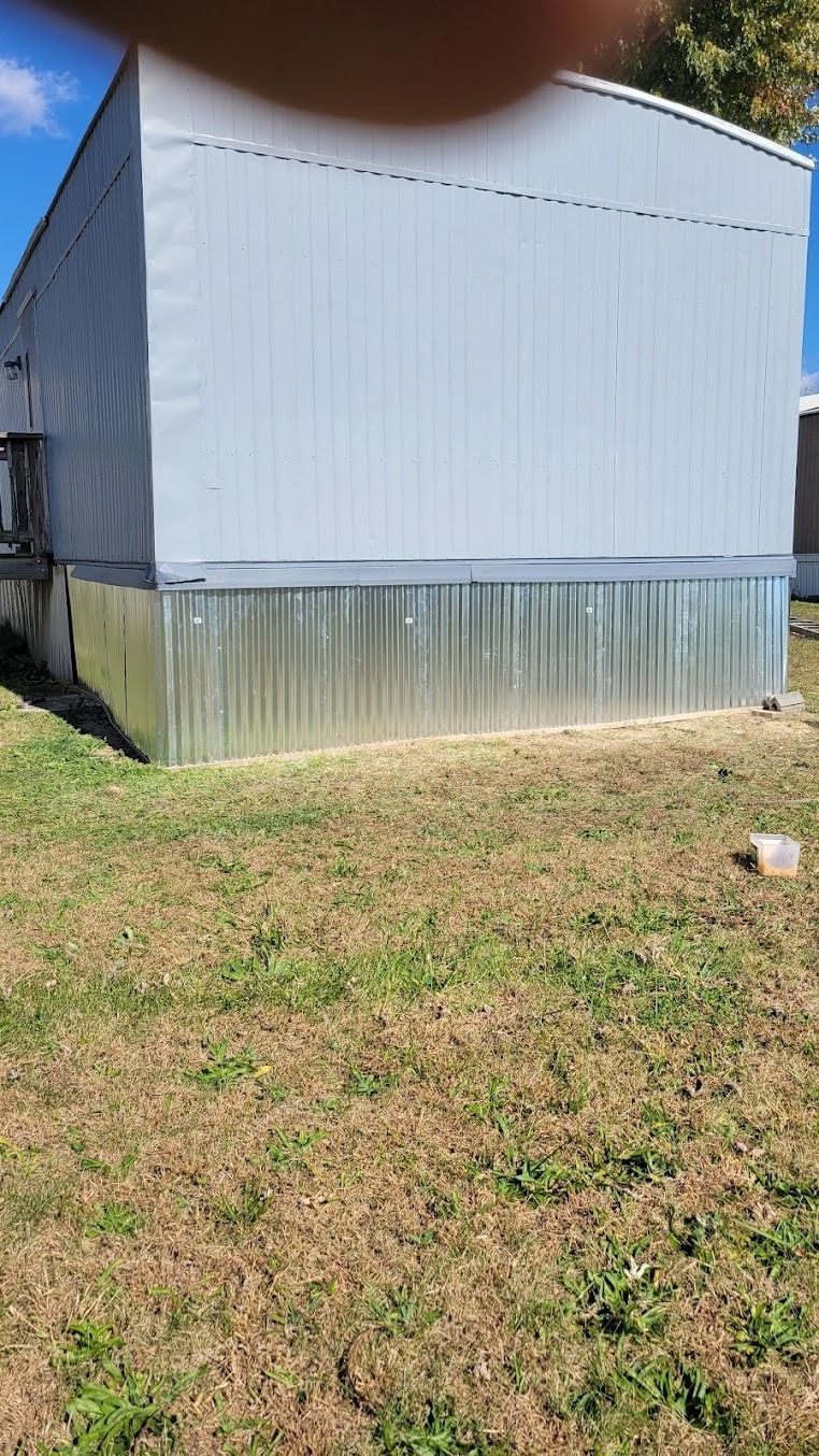 Light blue metal shed with a corrugated skirt, viewed on a grassy yard under a clear sky.