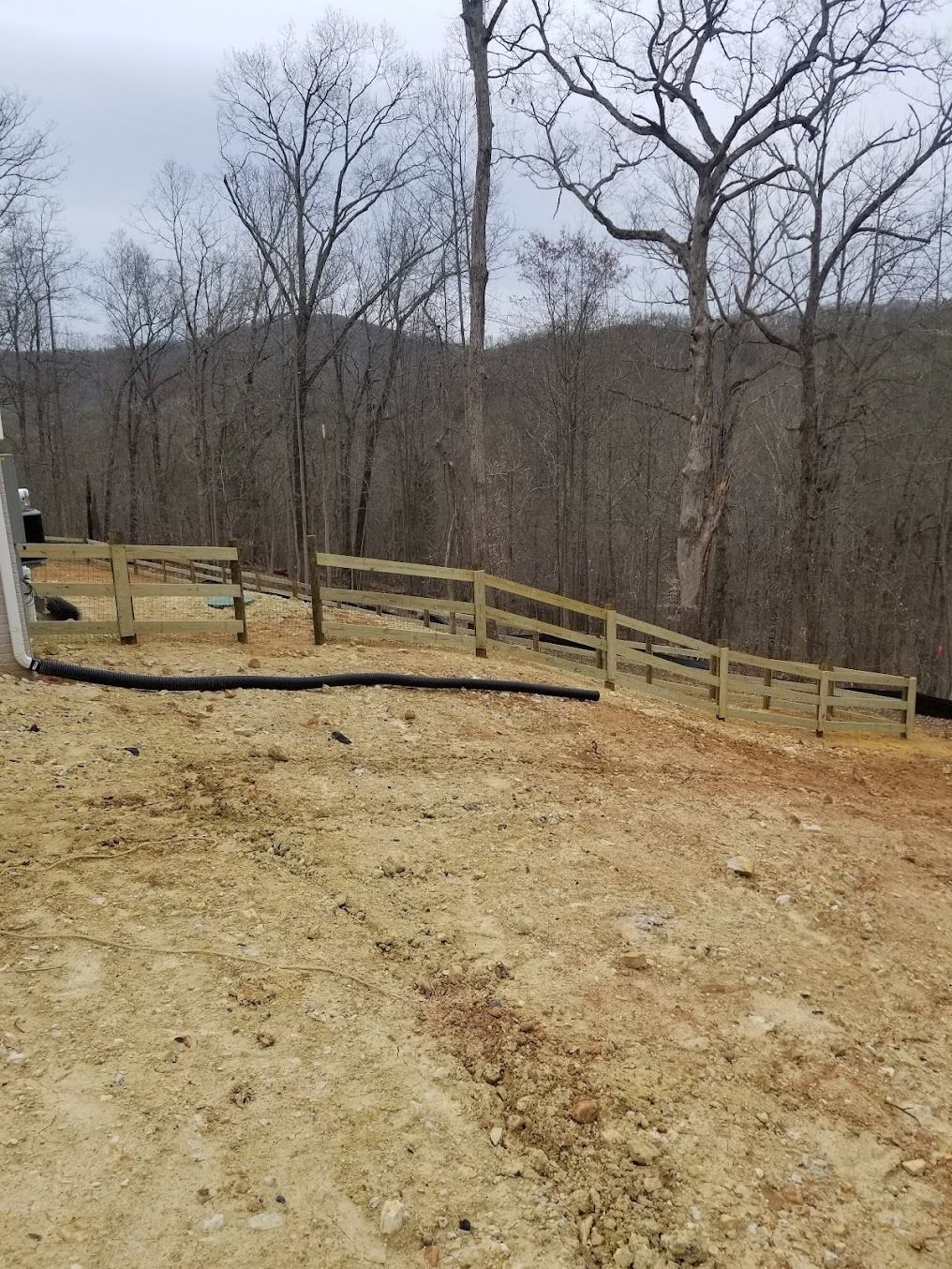 Wooden fence along a leafless hillside trail under cloudy winter trees