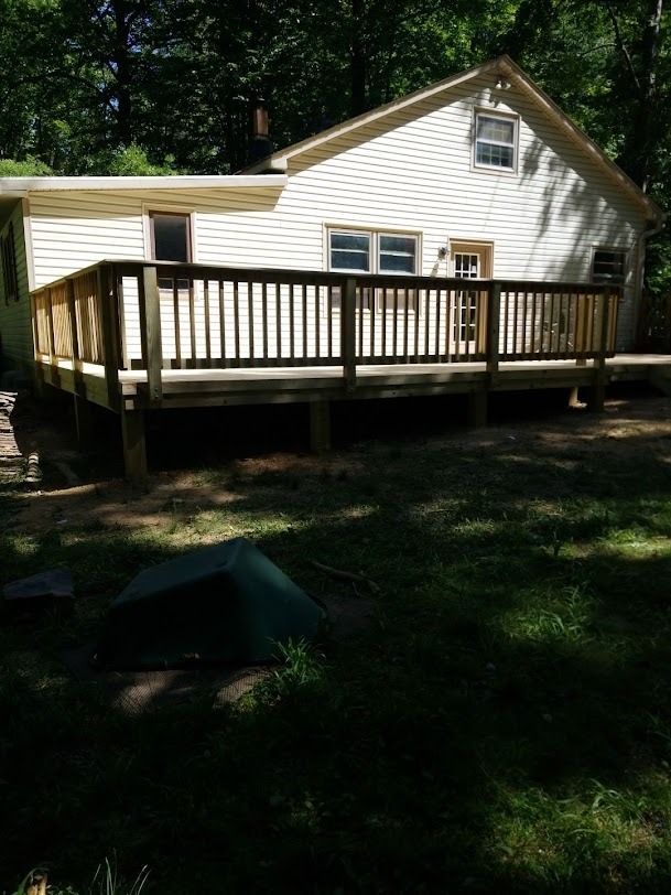 White house with a large wooden deck in a shaded yard