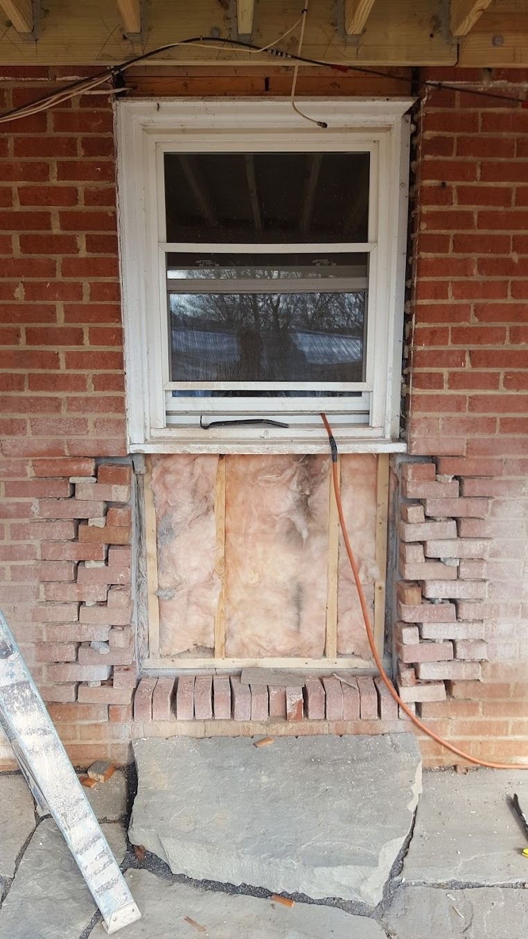 Exterior brick wall with a small window above a damaged, partially exposed wall opening
