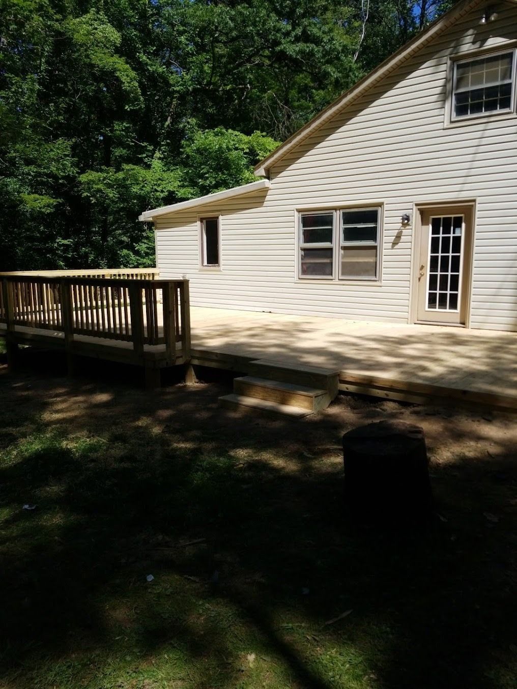 White house with deck and railing beside a wooded yard in bright sunlight